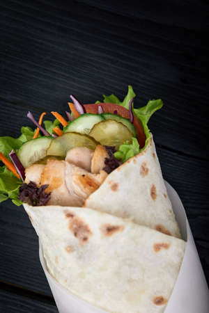 Shawarma rolled in lavash, moist grilled meat with onion, herbs and vegetables on wooden black background.の写真素材