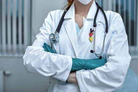 young beautiful woman doctor in white uniform and mask on her face with a stethoscope close up on clinic background.の写真素材