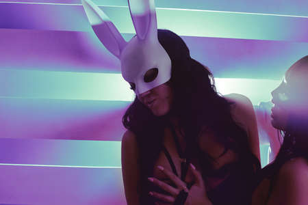 Sexy brunette masked rabbits kiss. LGBTQ concept, Girls in sexy outfits on the background of bright flashes of neon light. Fetish. Sexy woman in a boudoir. BDSM Sexual games of two girls.の写真素材