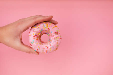 Female hand holding delicious donut on pink background, closeup.の写真素材
