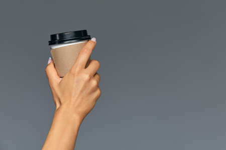 Hand of a girl holding a paper cup of coffee, gray background Good morning, concept. Empty place for an inscription.の写真素材