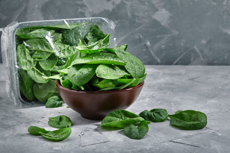 Fresh spinach in an old bowl on a gray background. Selective focus, horizontal. environmental...