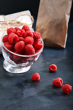 Fresh raspberries in a plate on a blue background. Food delivery concept, eco-friendly packaging....