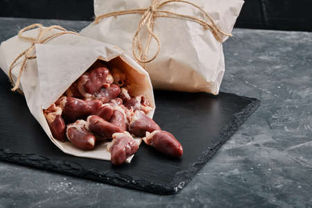 Raw chicken hearts wrapped in ecological packaging. Raw chicken meat on a gray cement background. Copy space, product deliveryの写真素材