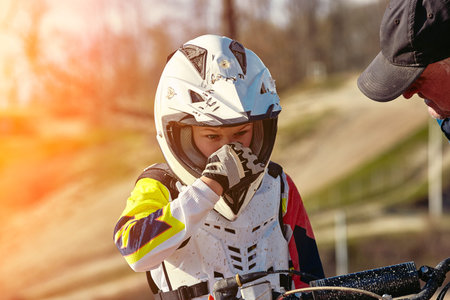 Portrait of boy dressed and equipped for motorbike racing sitting on motorcycle.