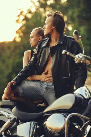 Young beautiful couple hipsters in stylish clothing for a retro motorcycle on the street, outdoor portrait, posing, in jeans and t-shirts, bearded guy, blonde girl, travel togetherの写真素材