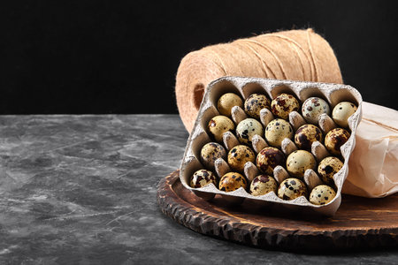 Quail eggs in a gray cardboard box. Close-up photo. Black concrete background. Healthy protein...