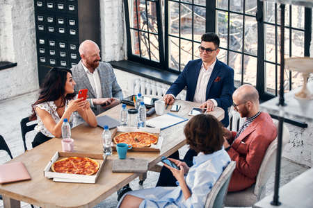 business, food, lunch and people concept - happy international business team eating pizza in officeの写真素材