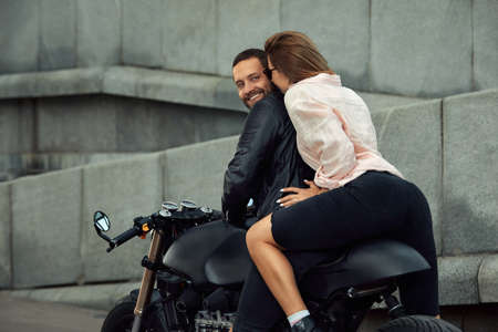 fashion couple sitting on a motorcycle, stone wall on the background. young man and woman with modern motorcycleの写真素材
