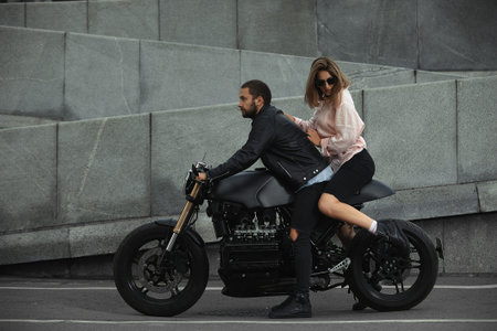 fashion couple sitting on a motorcycle, stone wall on the background. young man and woman with...