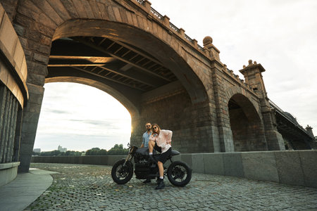 Young sexy woman hugging cute man in stylish black leather jacket, sitting on sports motorcycle...