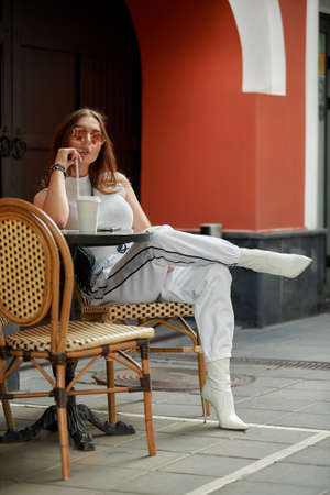 Stylish young brunette beauty having tasty refreshments in street coffee shop.の写真素材