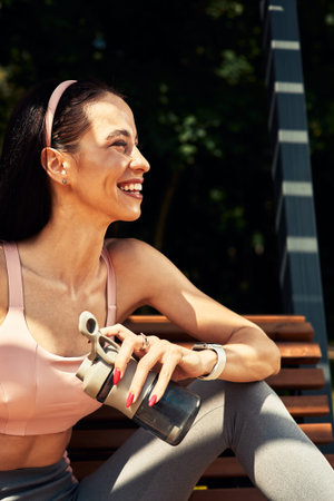 sports confident girl resting after workout outdoor and drinks water from a bottle, leads a healthy...