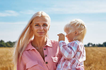 happy mother holding baby smiling on a wheat field in sunlightの写真素材