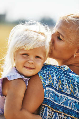 happy mother holding baby smiling on a wheat field in sunlightの写真素材