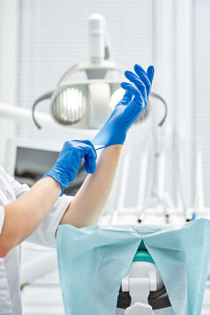 A female dentist puts on gloves against a background of dental equipment in a dental office. Happy patient and dentist concept.の写真素材