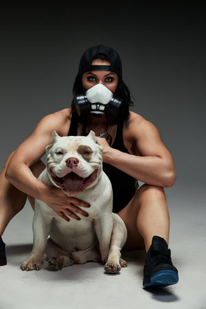 Young sporty woman in medical mask hugs her dog american bully. Pandemic. Coronavirus concept. Health protection during covid-19 outbreakの写真素材