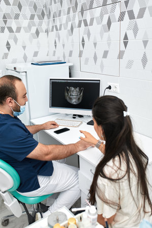 people, medicine, stomatology and health care concept - happy male dentist showing work plan to woman patient at dental clinic officeの写真素材