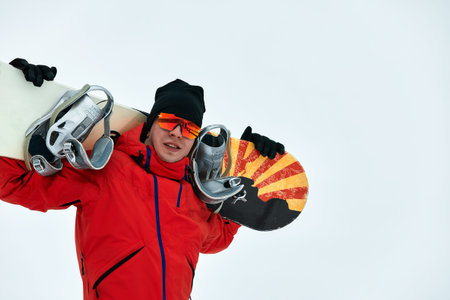 Male snowboarder in a red suit walking on the snowy hill with snowboard, Skiing and snowboarding conceptの写真素材