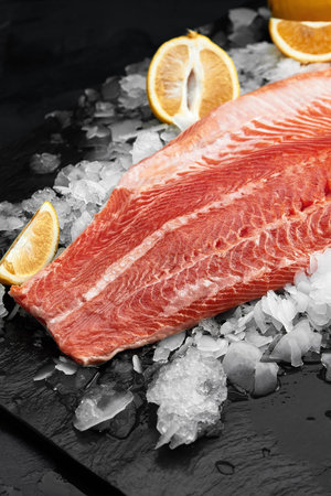 Lightly salted trout. Fresh fish fillet with culinary ingredients, herbs and lemon on a black...