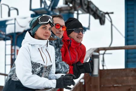 group of skiers friends on the mountain are resting and drinking coffee from a flask on the...
