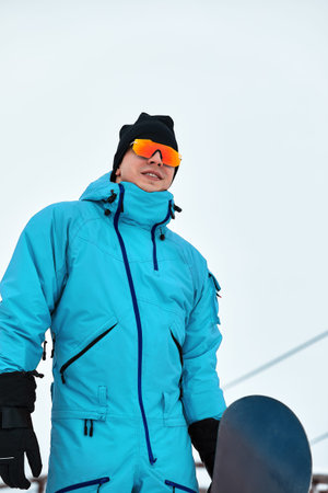Male snowboarder in a blue suit walking on the snowy hill with snowboard, Skiing and snowboarding...