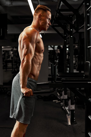 Man an athlete is engaged in a gym, doing an exercise on the muscles of the arms biceps black...