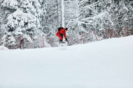 Male snowboarder in a red suit rides on the snowy hill with snowboard, Skiing and snowboarding conceptの写真素材