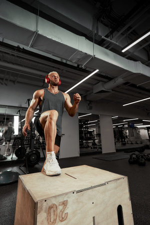 Sexy muscular men using the platform for his legs on a dark colorful background of gym.