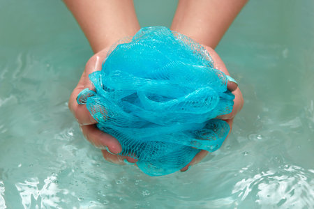 female hands holding a round soft synthetic washcloth in bath with water. Hands close-up. Spa...