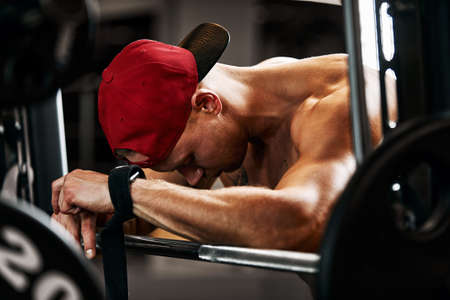 Closeup portrait of a muscular man workout with barbell at gym. Brutal bodybuilder athletic man with six pack, perfect abs, shoulders, biceps, triceps and chestの写真素材