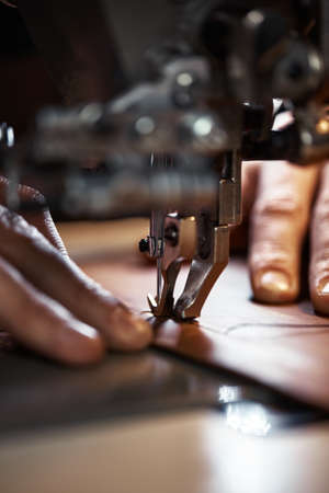 Working process of leather craftsman. Tanner or skinner sews leather on a special sewing machine, close up.worker sewing on the sewing machineの写真素材