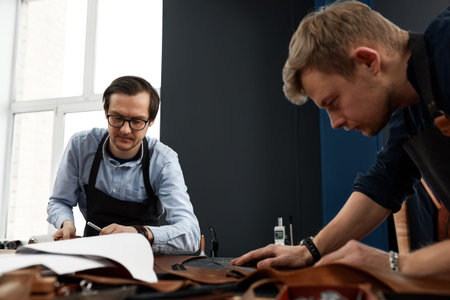 leather craftsmen working making measupenets in patterns at table in workshop studio