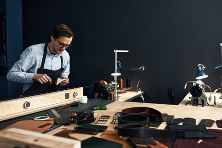 leather craftsmen working making measupenets in patterns at table in workshop studio