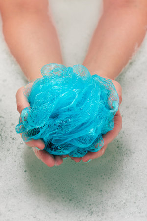 female hands holding a round soft synthetic washcloth in bath with water. Hands close-up. Spa treatment, body care, water backgroundの写真素材