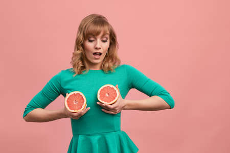 A middle-aged woman holds grapefruits on her chest, a blonde in a green dress with grapefruits in her hands. Healthy diet food, weight loss concept.の写真素材