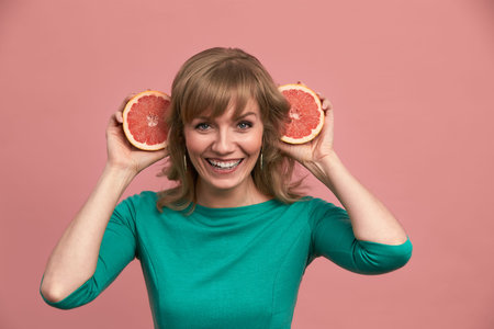 A beautiful girl with grapefruits in her hands, a blonde in a green dress holds halves of a grapefruit in her hands, beauty, vitamins, healthy skin.の写真素材
