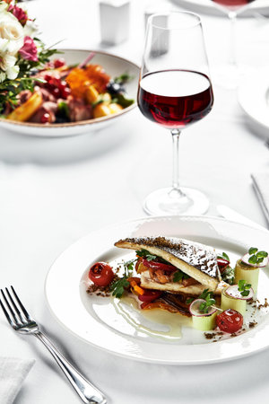 grilled sea bass with sauteed tomatoes, served with a potato ball on a white plate, sea bass fillet...