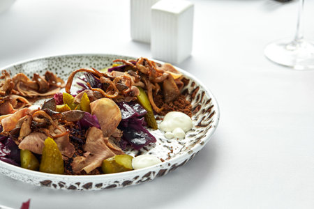 Thinly sliced beef tongue on a plate with fresh herbs and pickled cucumbers, close-up, light...