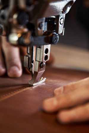 A sewing machine foot with the hands of a master close-up, a tailor makes a seam on a piece of...