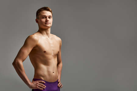 Young athlete swimmer in excellent physical shape looks at the camera, half-length portrait on a gray background, copy space, motivation for sports, advertising banner.の写真素材