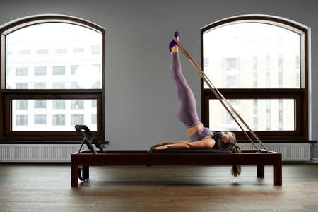 Modern equipment studio reformer for Pilates in the gym, Concept of recovery and rehabilitation, the instructor performs exercises on the studio reformer to correct the musculoskeletal system.の写真素材