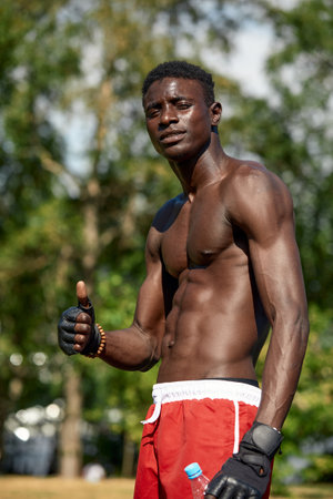 Shirtless african american man showing thumbs up, while training on the sports ground in the park, the athlete shows that he is doing fineの写真素材