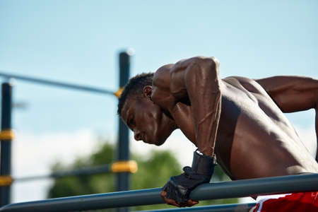 Black young man exercising on the uneven bars in the park, crossfit concept, african american man doing exercises on the uneven bars in the street, on the sports groundの写真素材