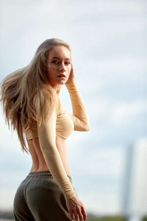 A beautiful woman, blonde, fitness instructor, in light clothes, trains on the beach, against the backdrop of the city. Shows exercises from yoga, pilates, deep work, step aerobics.の写真素材