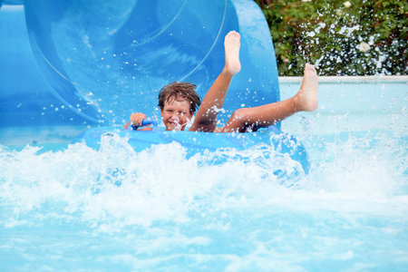 happy an 8 year old boy is riding in the water Park on inflatable circles on water slides with splashの写真素材