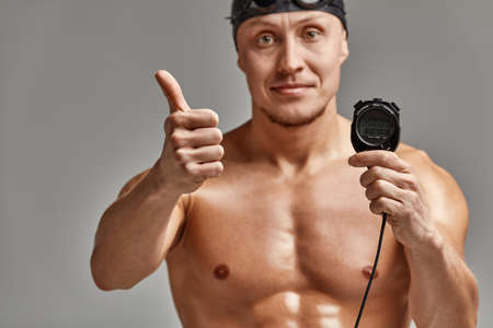 A coach with a stopwatch in his hands, a sports swimming coach with a timer in his hands, gray background, copy space.の写真素材