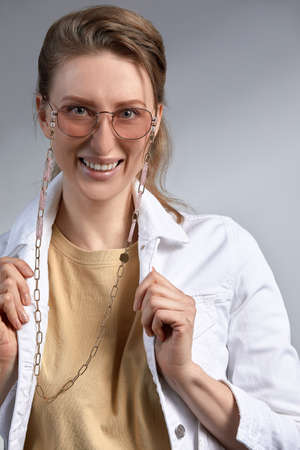 A beautiful stylishly dressed middle-aged woman in stylish glasses smiles and poses at the camera, a woman 35-45 years old blonde with good, healthy skin in glasses on a gray background.の写真素材