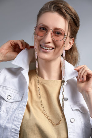 A beautiful stylishly dressed middle-aged woman in stylish glasses smiles and poses at the camera, a woman 35-45 years old blonde with good, healthy skin in glasses on a gray background.の写真素材