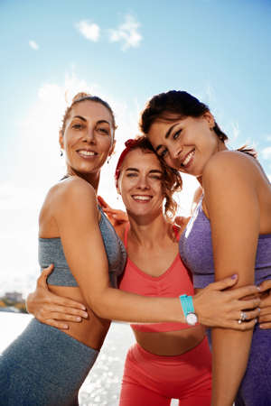 Happy women in fitness clothes relaxing and having fun in the park by the river. Fitness, sport, friendship and healthy lifestyle concept . Group of happy people exercisingの写真素材